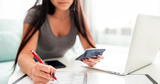 Uma mulher sentada em uma mesa, usando um laptop, caneta e calculadora para declarar o imposto de renda
