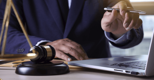 Profissional em seu laptop e balanças da justiça ao lado simbolizando o leilão eletrônico